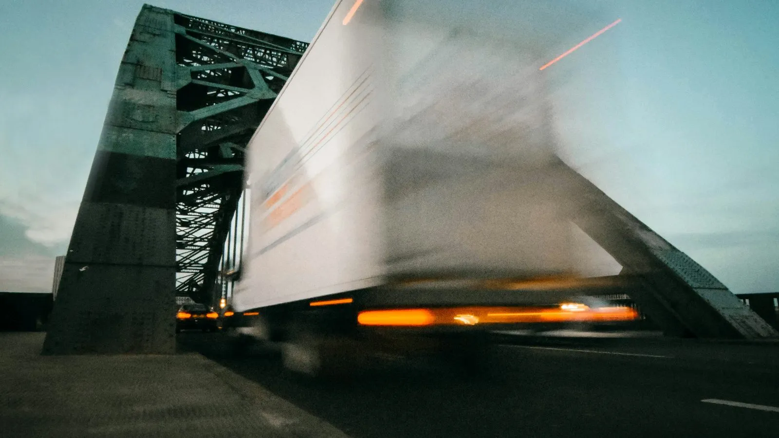 White truck crossing a steel bridge at dusk with motion blur
